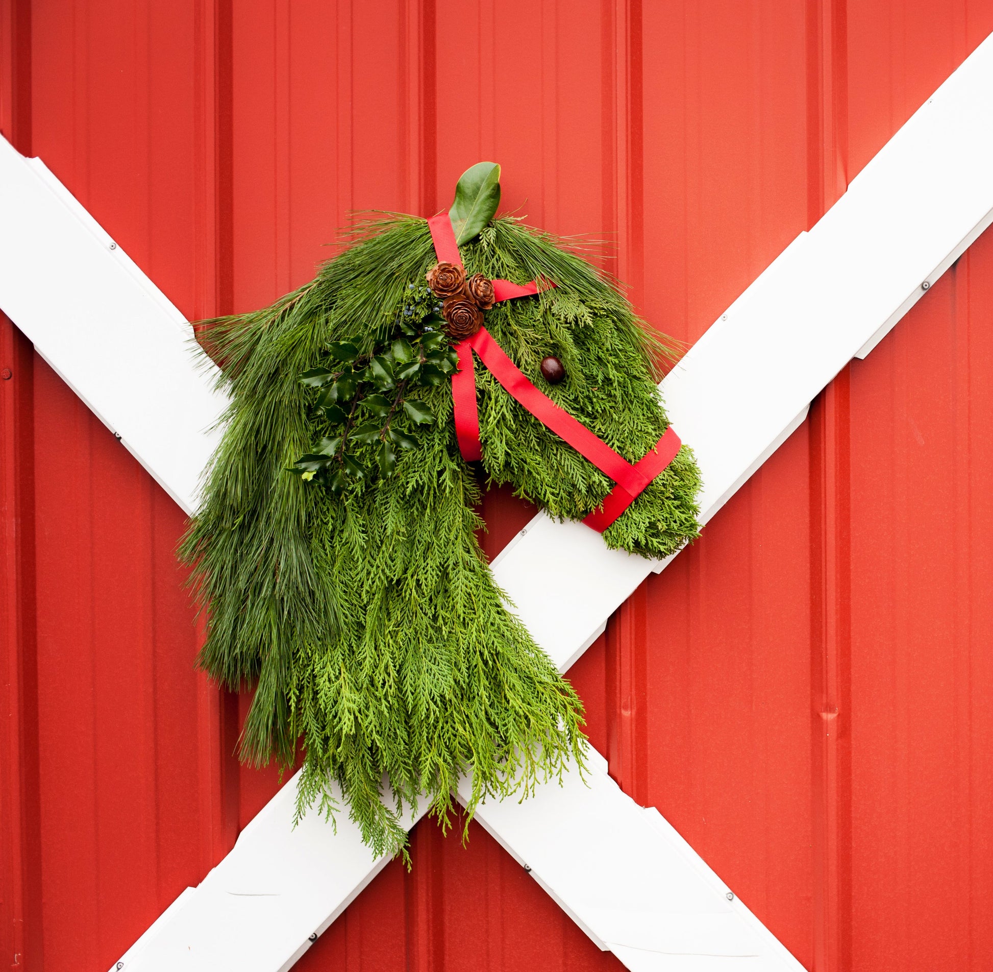 Green wreath shaped like a horse head on a red barn door with white crossbar